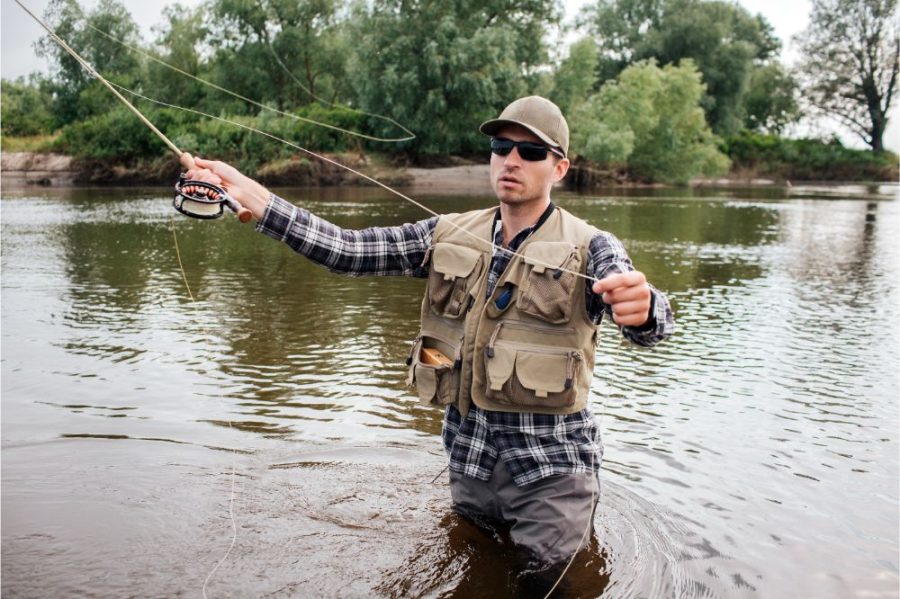 Man in sunglasses stands in water and fishing.
